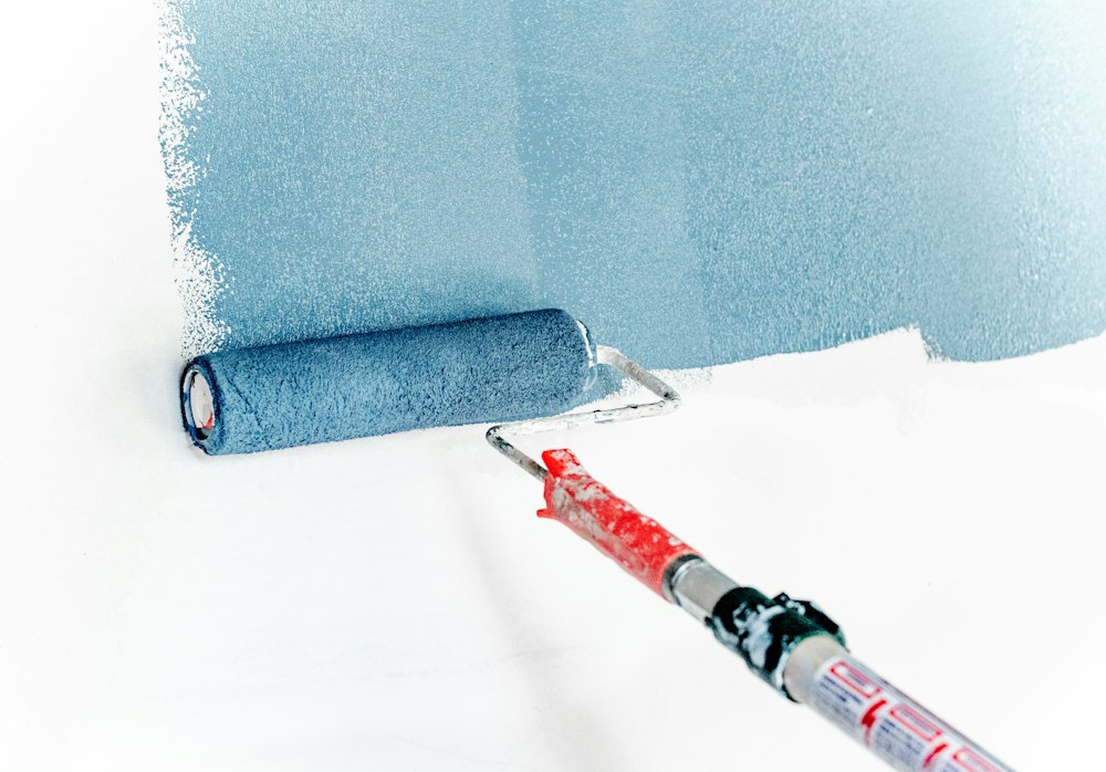 Paint roller applying a fresh coat of blue paint to an interior wall